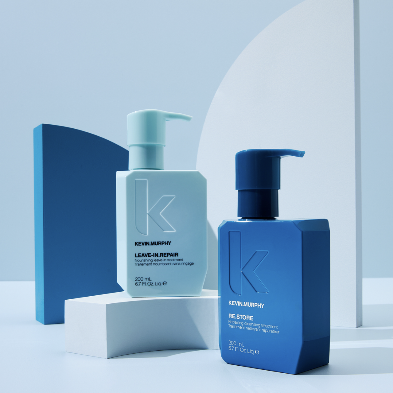 Product shot featuring two Kevin Murphy hair care bottles in light and dark blue hues, set against a geometric background.