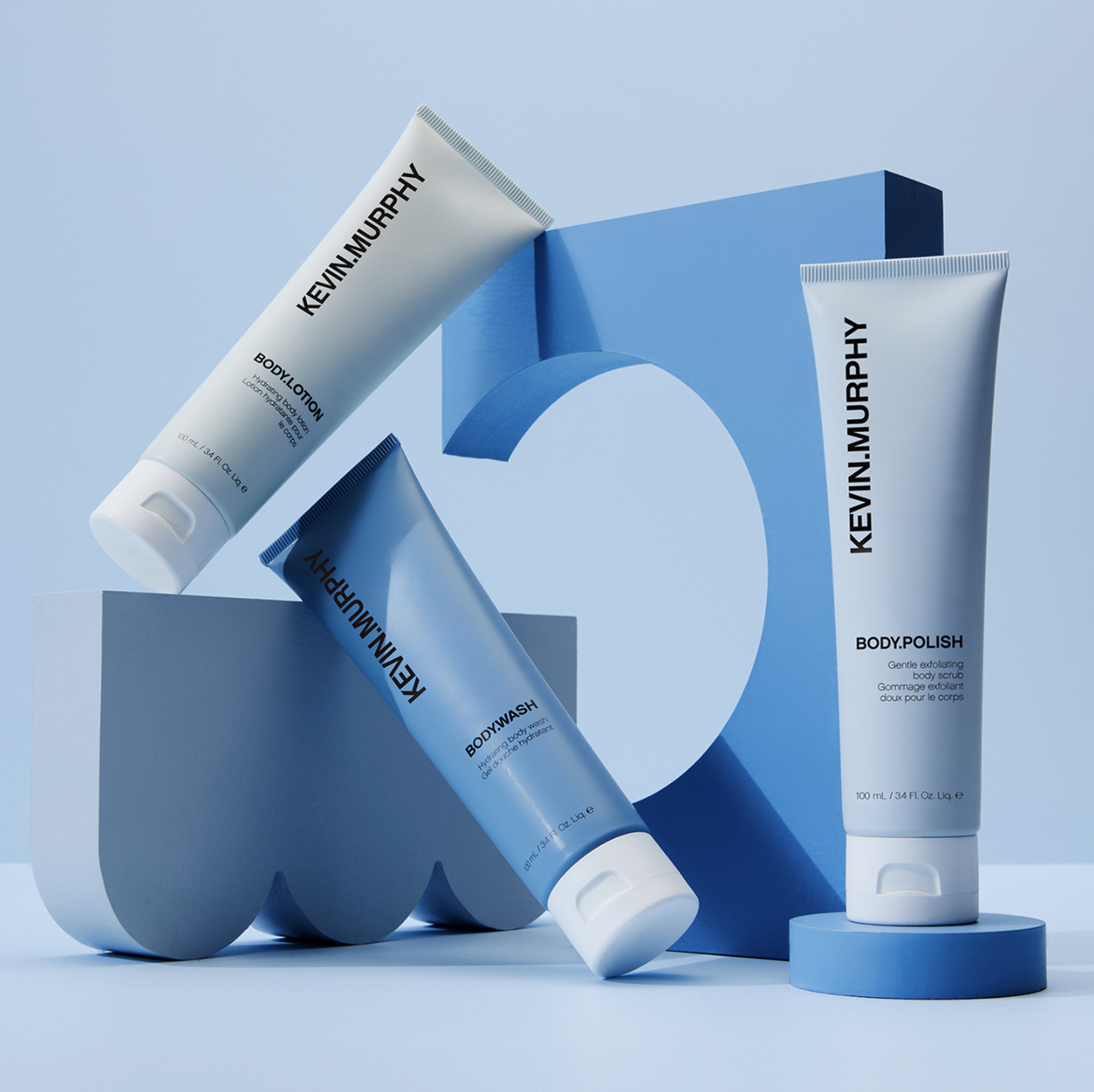 Still life of Kevin Murphy brand body lotions and body wash products in blue and white packaging on a light blue background.