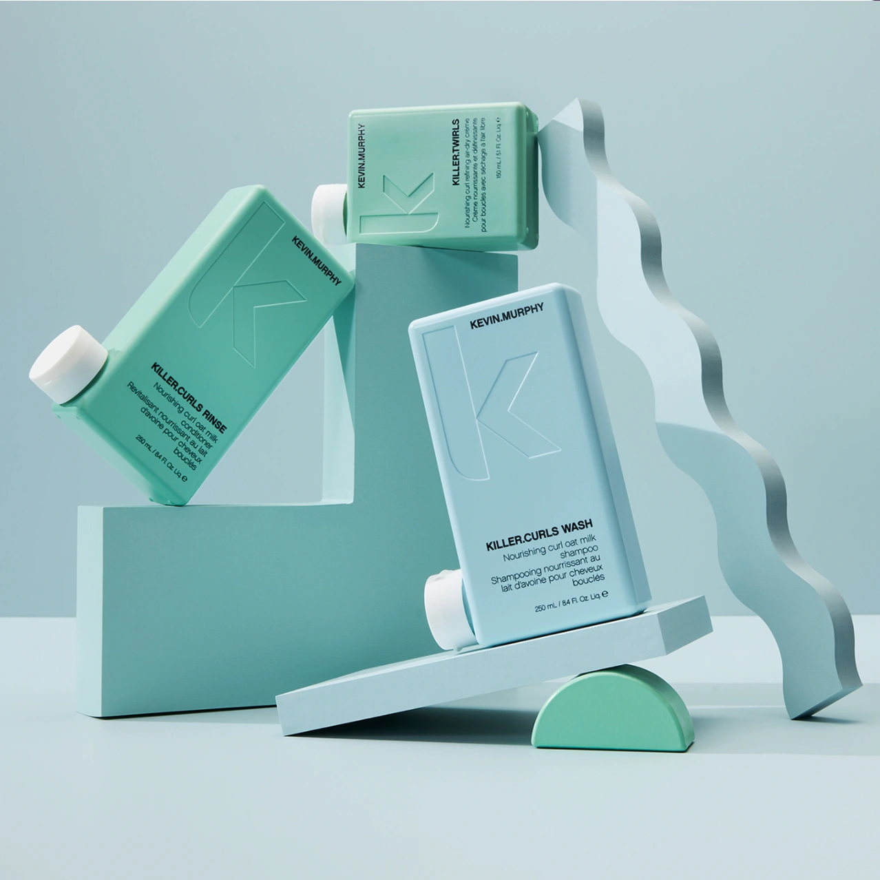 Kevin Murphy hair product bottles arranged on pastel teal and blue geometric sculptural blocks against a light background