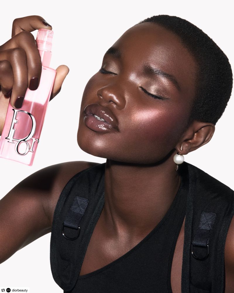 Model Akon Changkou with glowing makeup holding a pink Dior mist bottle against a white studio background.