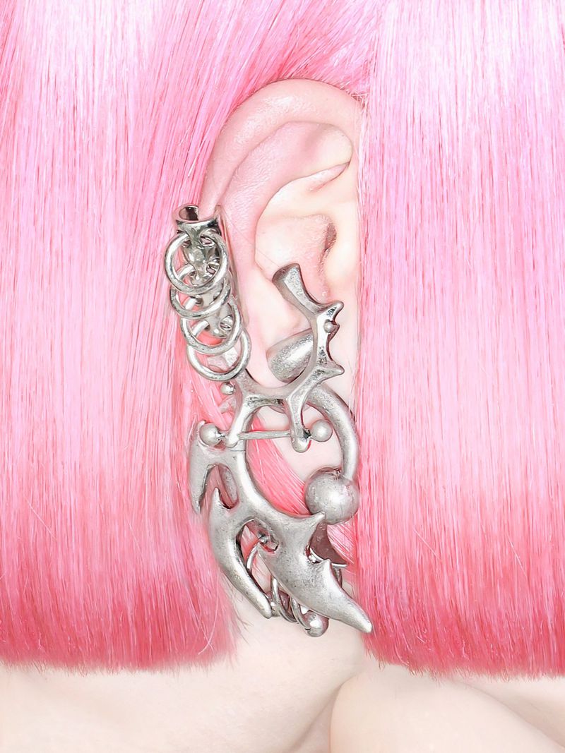 Close-up of an intricate silver sculptural ear cuff worn on an ear framed by vibrant pink hair.
