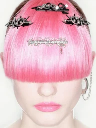 Close-up portrait of a model with blunt pink bangs covering her eyes, styled with silver metallic hair clips and a handcuff earring.