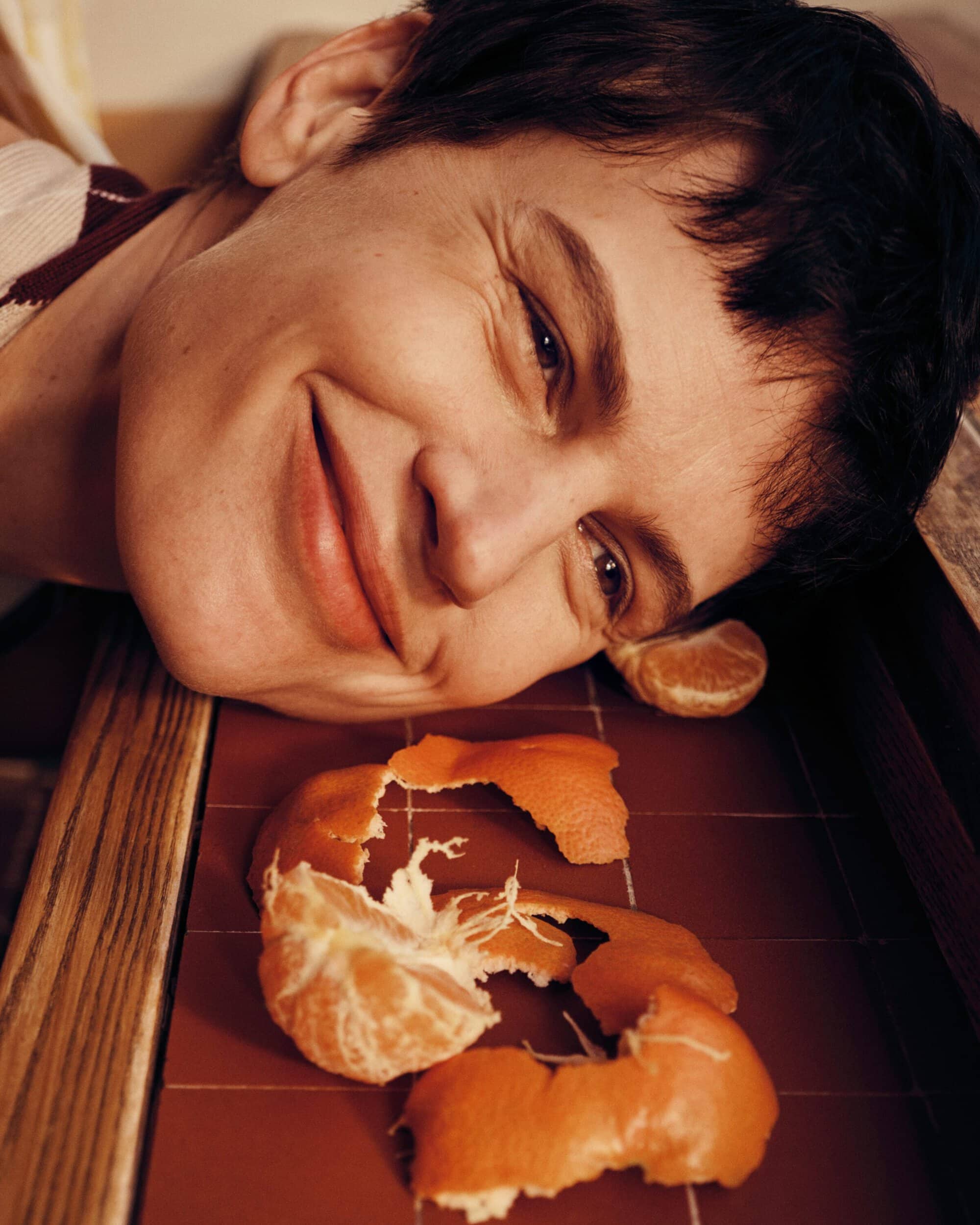 Close-up of model Saskia de Brauw resting her head on a tiled surface next to peeled orange slices and rinds.