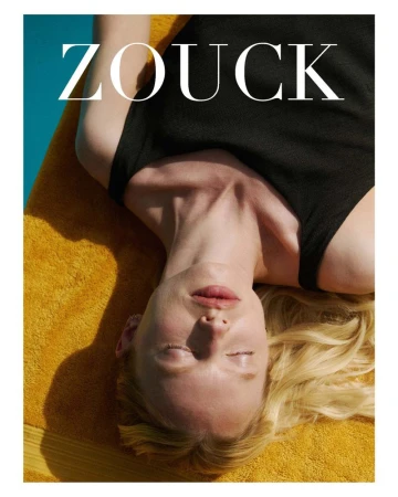 Model India Tuersley lying back on a yellow towel in a black tank top under bright sunlight next to a pool.
