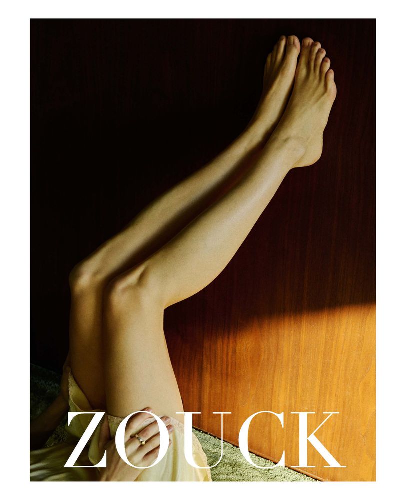 Model India Tuersley's bare legs raised upwards against a warm wood paneled wall in sharp directional sunlight.