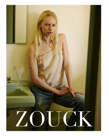 India Tuersley wearing a cream lace camisole and denim jeans seated beside a vintage green sink in a bathroom.