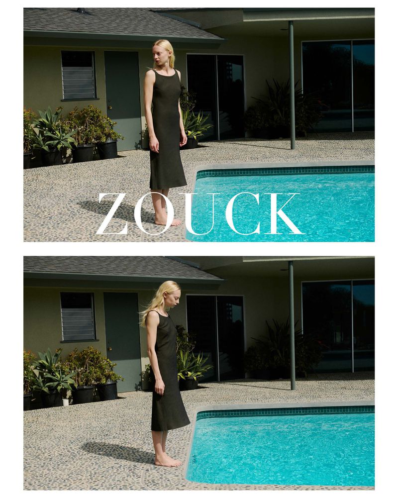 Model India Tuersley wearing a dark sleeveless midi dress while standing barefoot next to a turquoise swimming pool for Zouck.