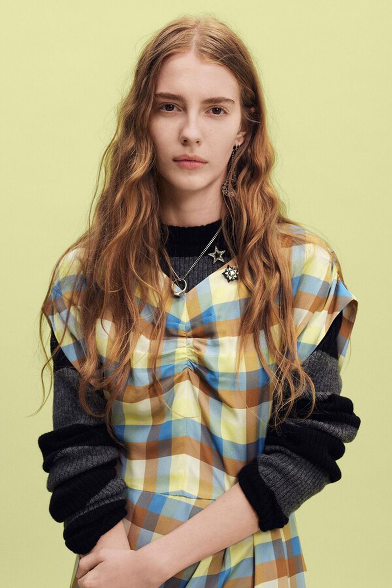 Model with long wavy blonde hair wearing a plaid dress and star necklace against a light background