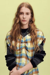 Model with long wavy blonde hair wearing a plaid dress and star necklace against a light background