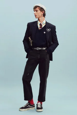Model wearing a dark blazer, dark jeans, white beret cap, and black sneakers against a pale blue seamless backdrop.