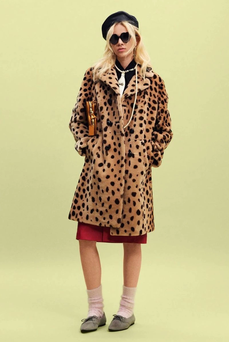 Model in a leopard print coat, black beret, and sunglasses posing against a pale green backdrop.