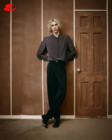 Full-length portrait of a blond male adult fashion model posing in a studio with a brown wall and a painted brown door.