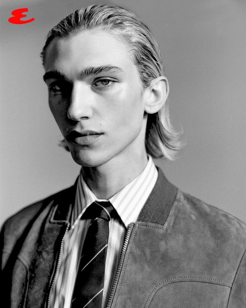 Black and white portrait of a young adult male with light skin, wearing a jacket, dress shirt, and tie, looking at the camera.
