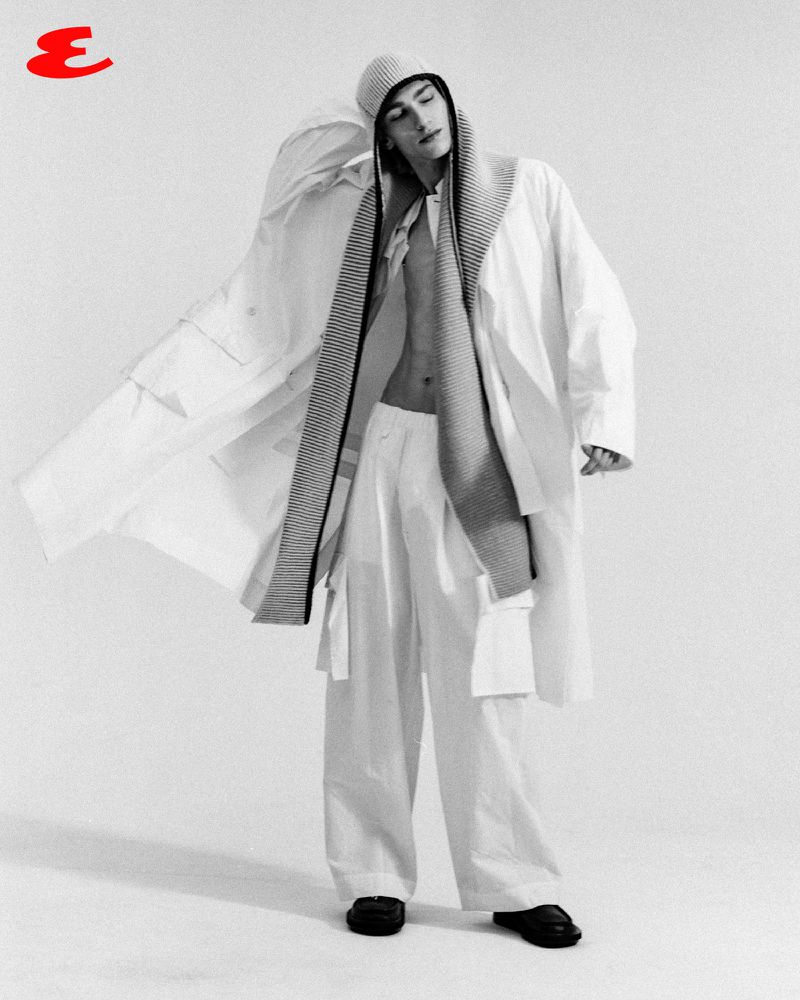 Noah Hanes wearing an open oversized white coat, wide-leg trousers, and a knit hood against a white studio background.