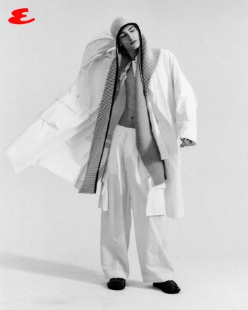 Noah Hanes wearing an open oversized white coat, wide-leg trousers, and a knit hood against a white studio background.