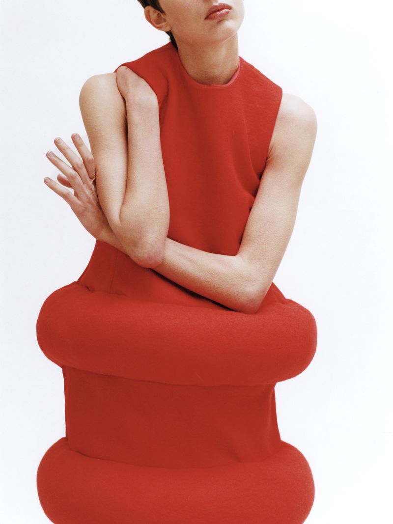 Woman in red dress with bulbous design poses against a white background, creating a striking fashion image.
