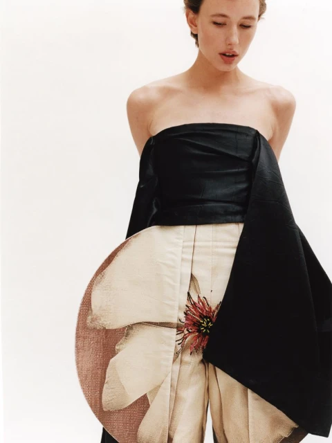 A fair-skinned woman poses in a strapless black and beige floral dress against a white backdrop, highlighting the dress's unique design and detail.