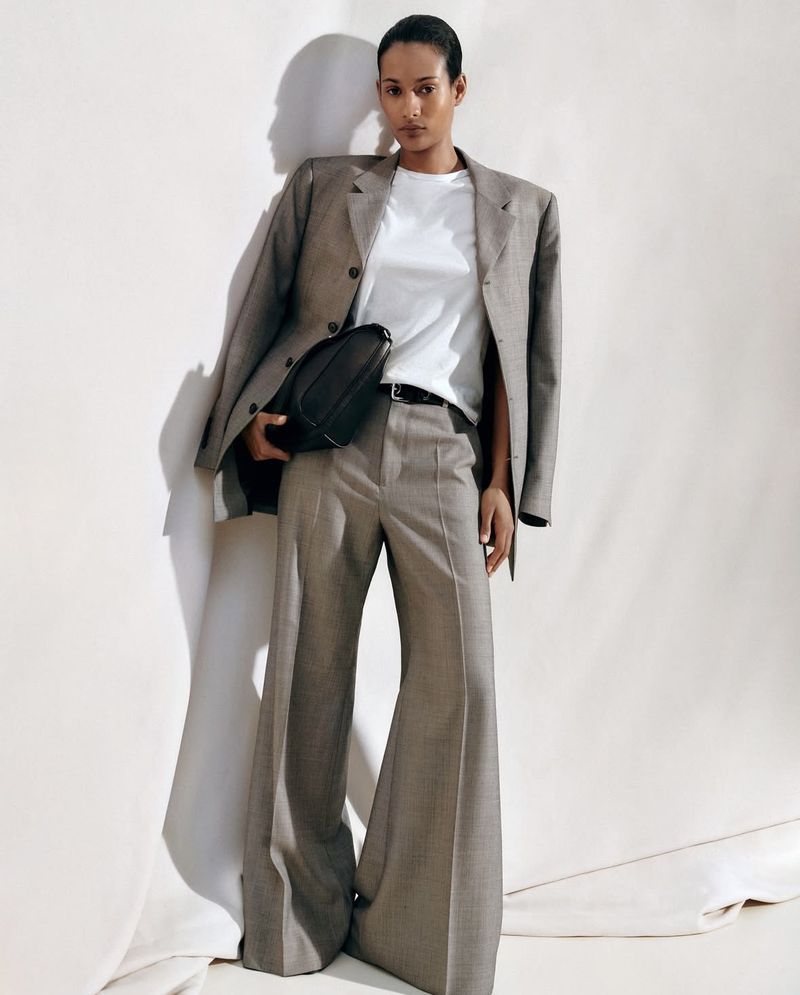Model Mar G wearing an oversized grey tailored suit with wide-leg trousers and a white t-shirt against a light studio backdrop.