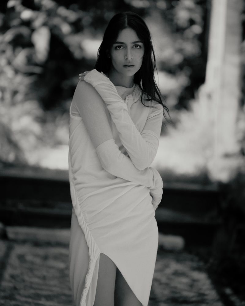 Model Nora Attal poses in a ruched draped white dress in a monochrome outdoor fashion portrait.