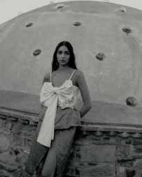 Model Nora Attal posing against a traditional stone dome structure wearing a bow-accented top and layered skirt in black and white.