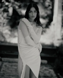 Model Nora Attal poses in a ruched draped white dress in a monochrome outdoor fashion portrait.
