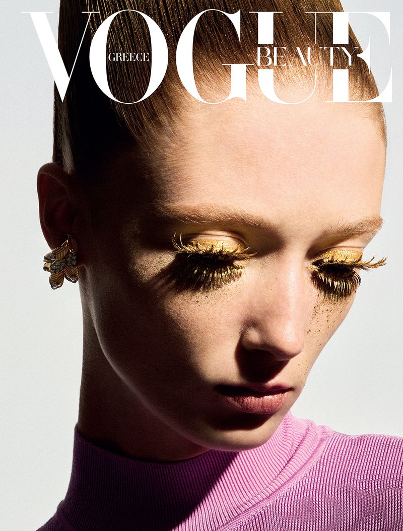 Vogue Greece beauty cover featuring a close-up of a woman with gold eyeshadow and eyelashes wearing a pink turtleneck sweater.