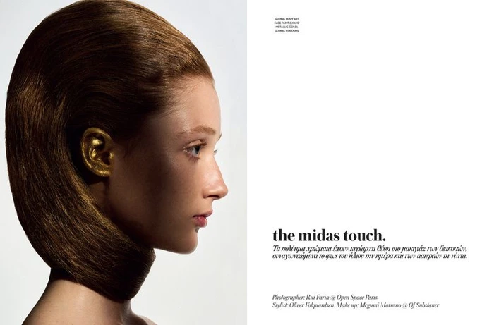 Profile portrait of a woman with sculpted brown hair and metallic gold paint on her ear against a white background