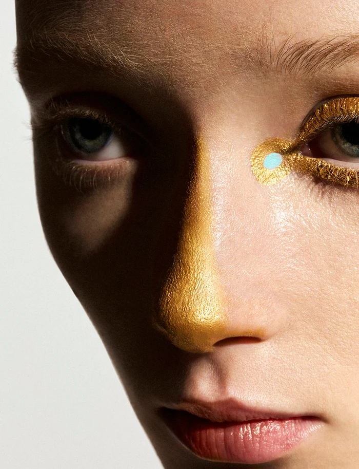 Close-up portrait of a model with metallic gold face paint on her nose and eyelids for Vogue Greece