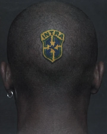 Back of a person's shaved head featuring an Intra crest dyed into the buzzcut, wearing a silver hoop earring against a dark background.