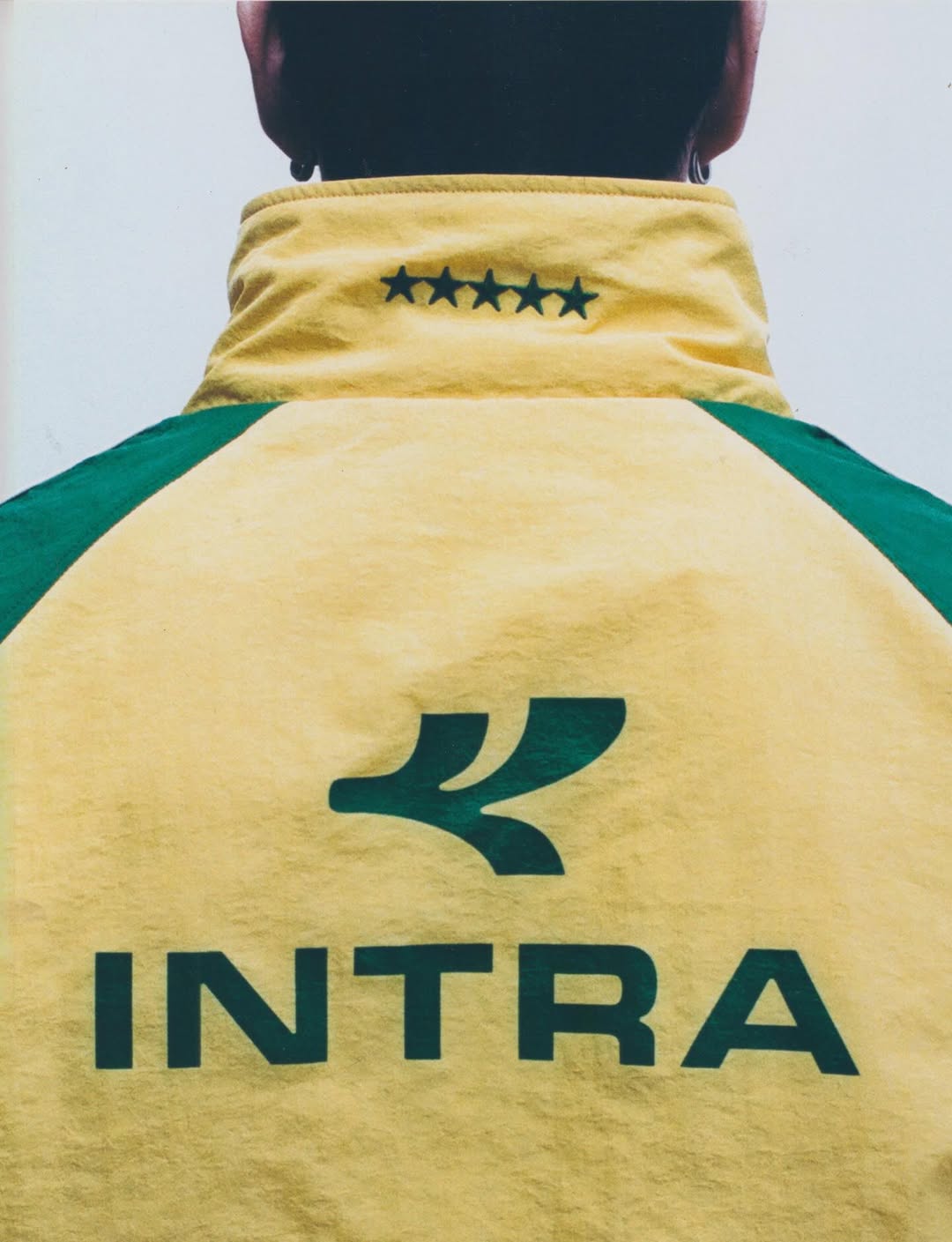 Back view of a person wearing a yellow and green Intra athletic jacket with printed logo and five stars along the high collar.