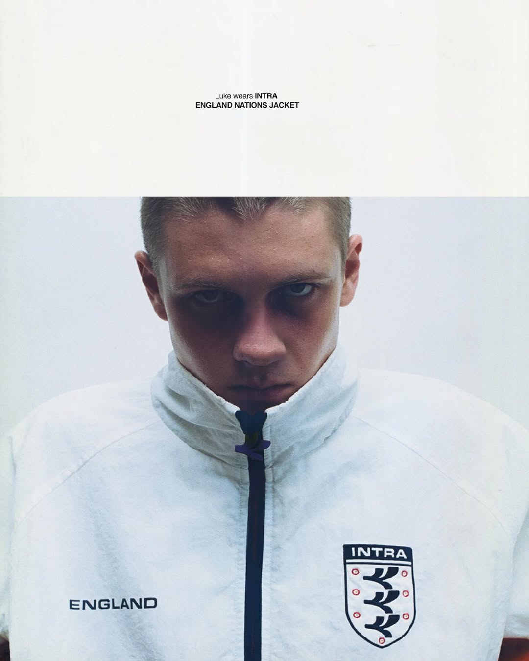 Close-up portrait of a man in a white Intra England Nations zip-up jacket against a white studio background.
