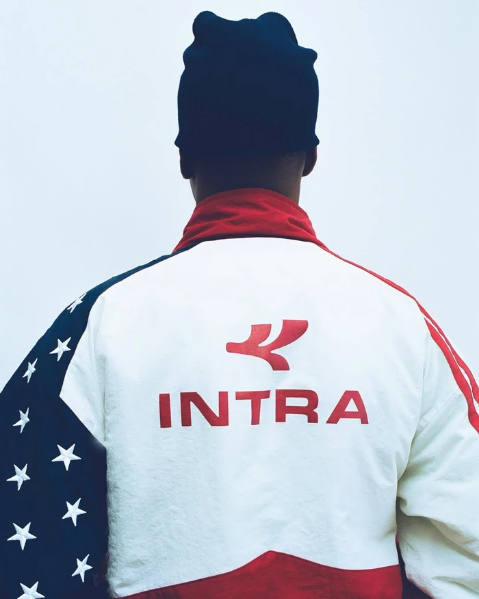 Rear view of a person wearing a black beanie and a white, red, and starry blue Intra athletic jacket.