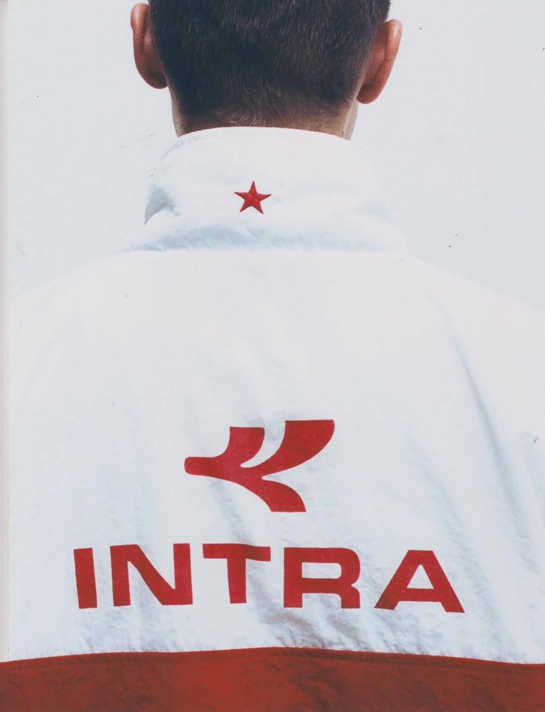 Rear close-up view of a model wearing a white Intra athletic jacket with a red star and logo printed across the back.