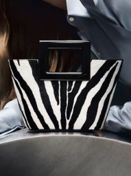 Marina Raphael zebra print tote bag with a black rectangular handle held against a pale blue satin shirt.
