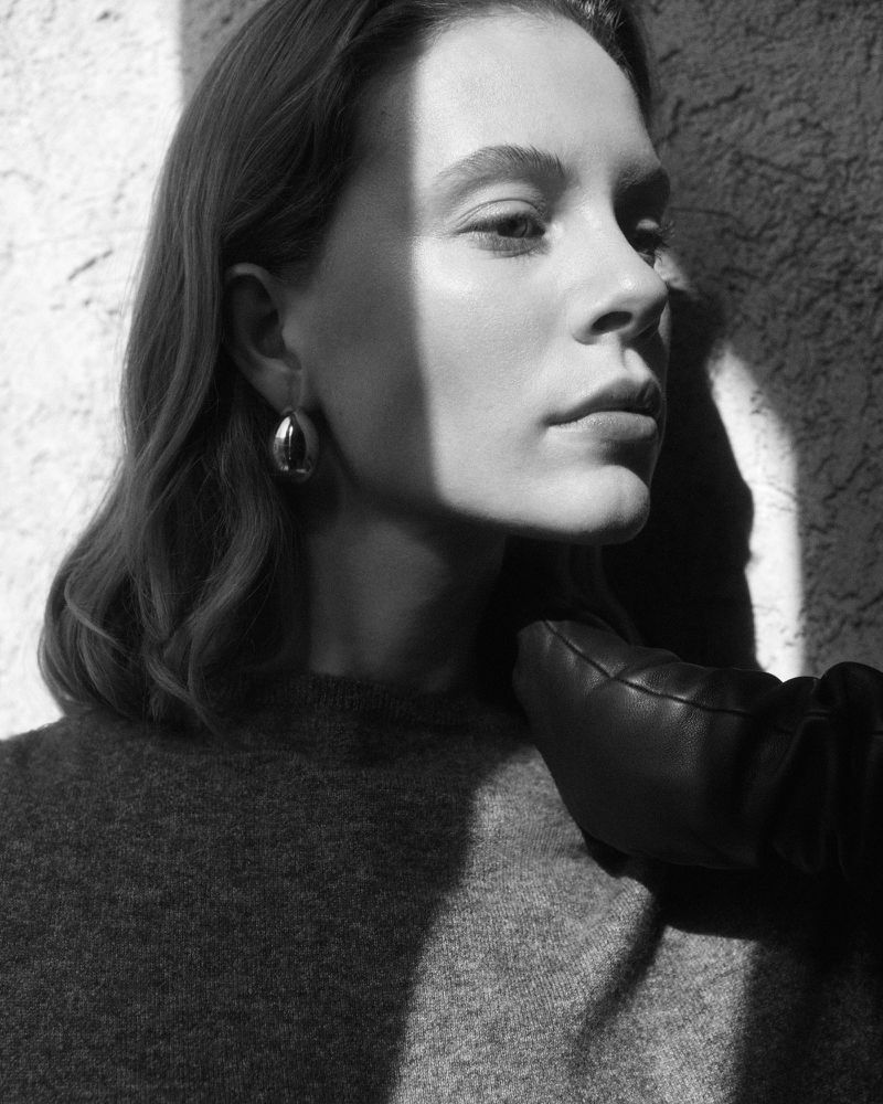 Black and white portrait of a woman with earrings and a gloved hand near her neck, capturing light and shadow on textured backdrop.