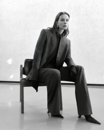Model seated on a chair wearing a tailored grey suit and dark gloves for Giada FW Pre Fall campaign.