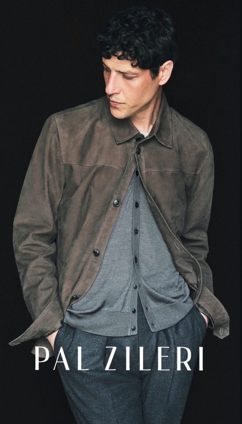 Model wearing a brown suede jacket, grey buttoned cardigan, and charcoal trousers against a black studio background.