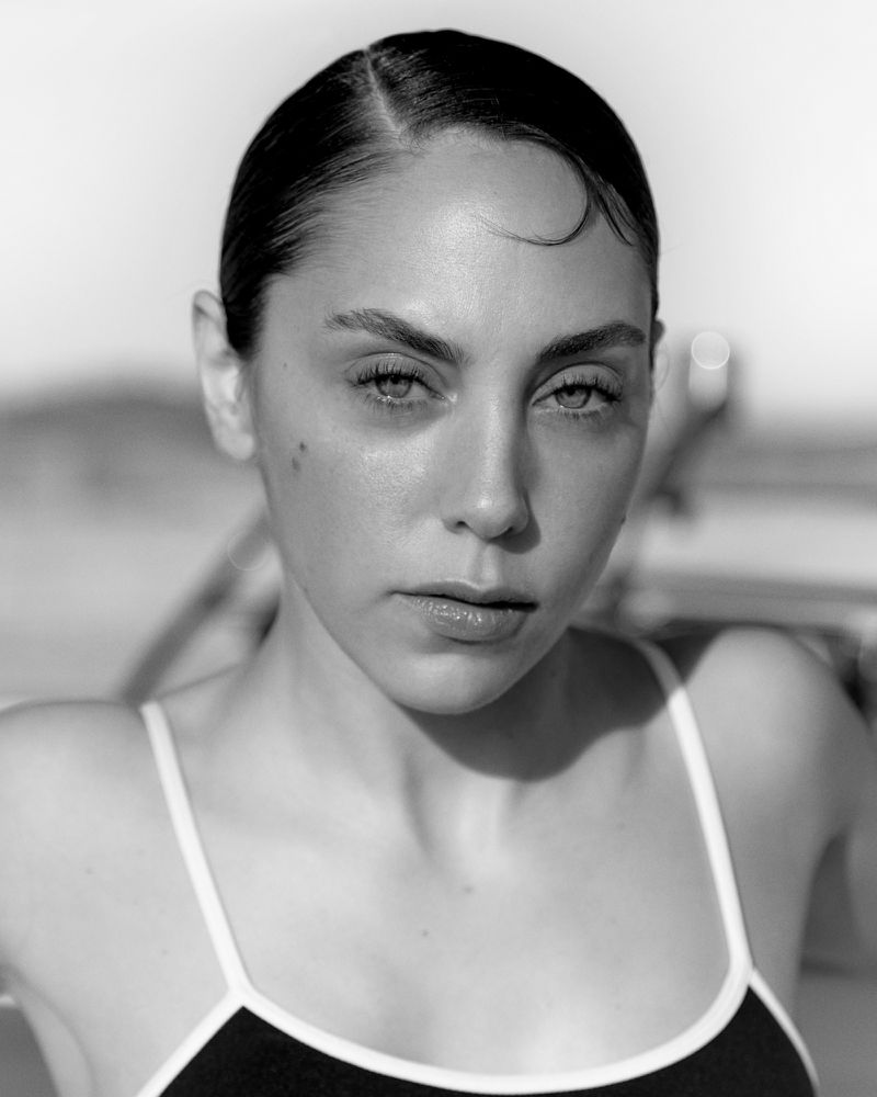Monochrome portrait of a young woman with slicked-back hair, wearing a camisole top. The image is a close-up with a shallow depth of field.
