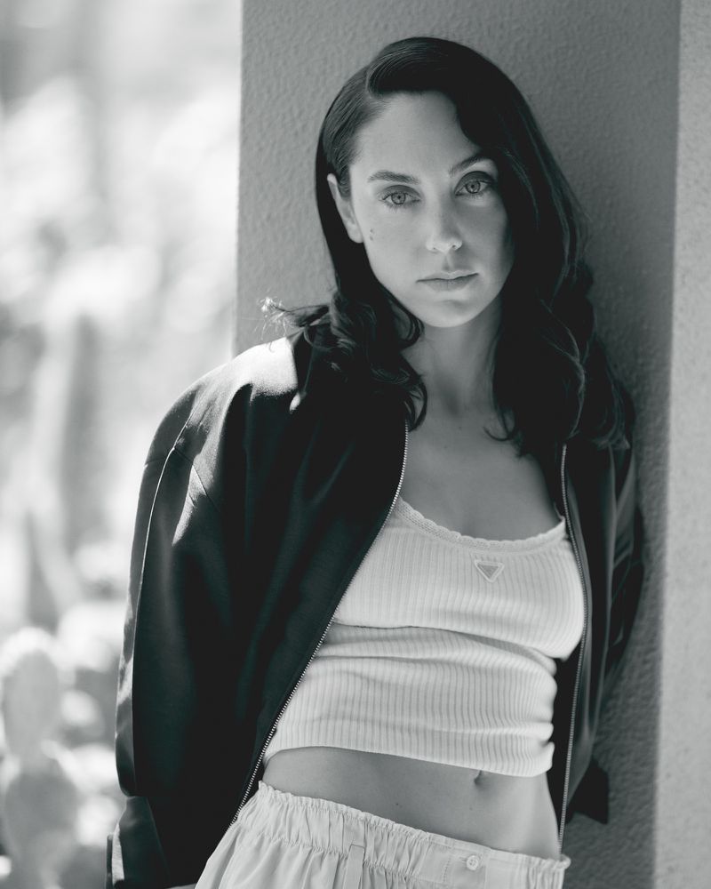 Black and white portrait of a woman with dark hair leaning against an architectural column in a fashion editorial
