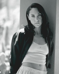 Black and white portrait of a woman with dark hair leaning against an architectural column in a fashion editorial