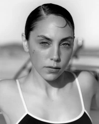 Monochrome portrait of a woman with dark slicked-back hair wearing a dark top with thin white straps.