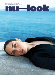 A woman in a black shirt lying down outdoors near the ocean for NU-LOOK Issue 6