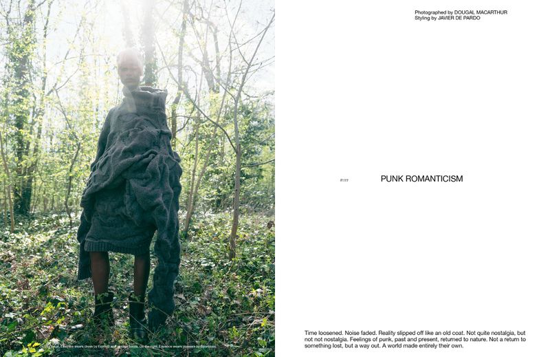 Fashion shot of a model wearing oversized sweater and boots in a forest setting with dappled sunlight and natural, editorial style.