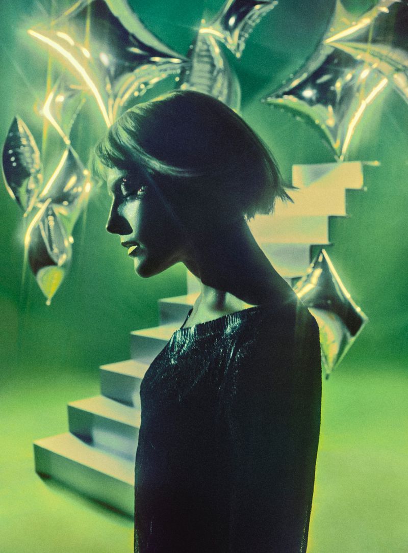 Profile of Mala Emde with a short bob haircut against a green studio backdrop with silver foil star balloons and stairs.