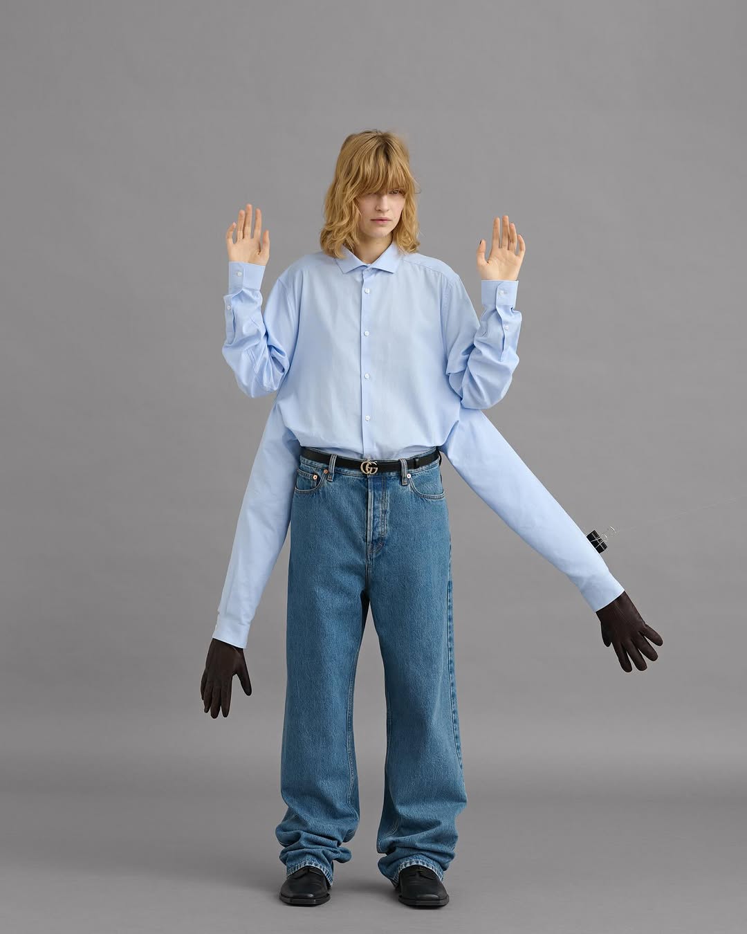 Model wearing a light blue multi-sleeve button-down shirt and blue jeans against a grey seamless background