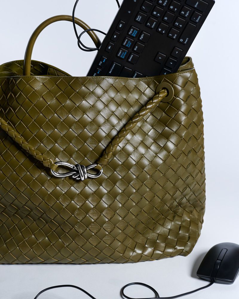 Olive green woven leather tote bag with keyboard and mouse on a white surface in a studio setting, product photography.