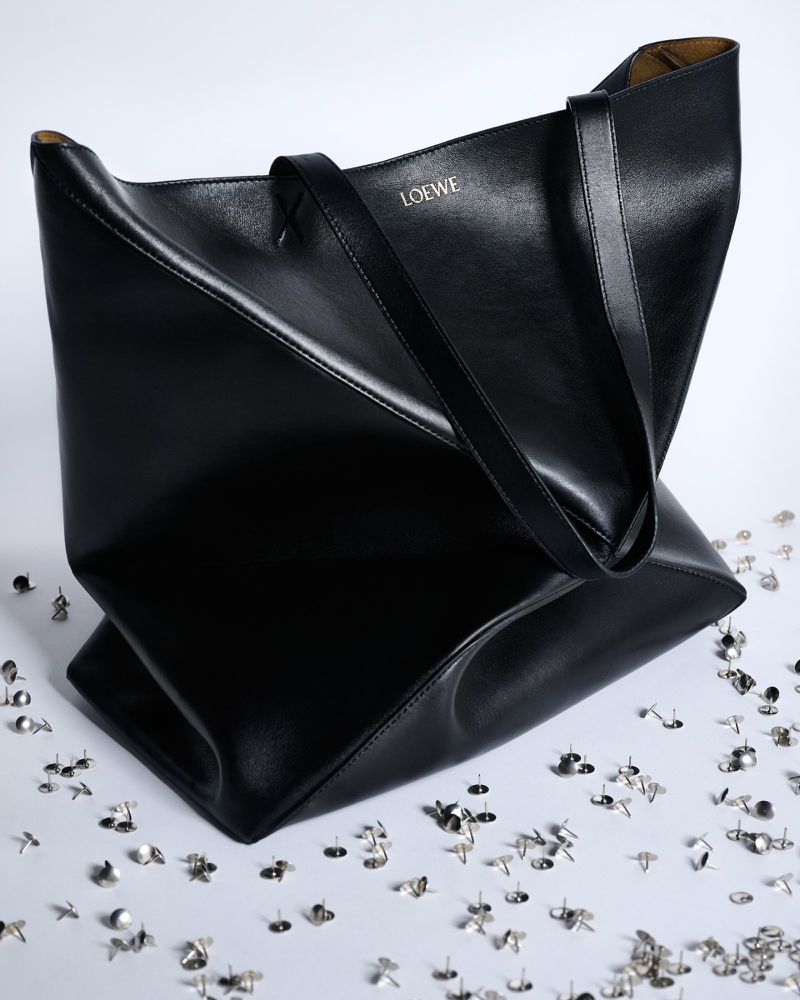 Black Loewe leather tote bag displayed on a white surface with silver push pins scattered around it, studio lighting, product photography.