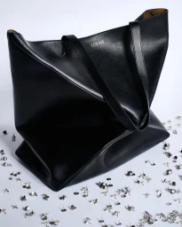 Black leather Loewe tote bag surrounded by scattered silver push pins on a seamless white surface.