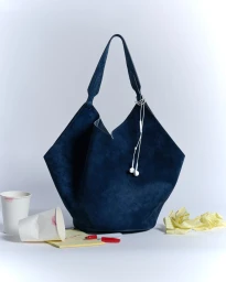 Dark blue suede tote bag with wired earphones, paper coffee cups with lipstick stains, and notepad on white background.
