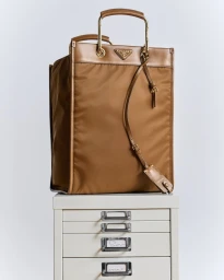 Brown structured tote bag resting on top of a white metal office filing cabinet in a brightly lit studio setting.